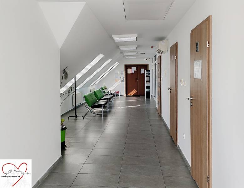 A hallway in offices with white walls, green chairs, and tiles.