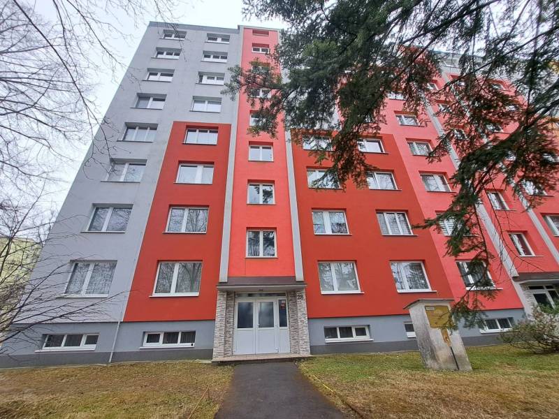 An apartment building in Poprad with a red facade, in front of which there is a sidewalk and trees.