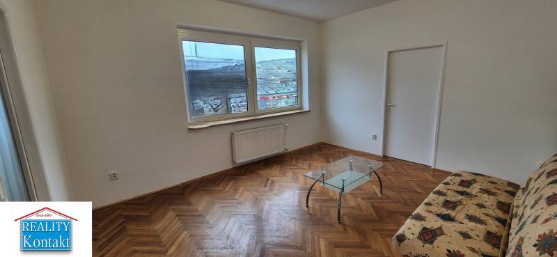 Living room with a sofa, glass table, and wood-patterned flooring in a three-room apartment.