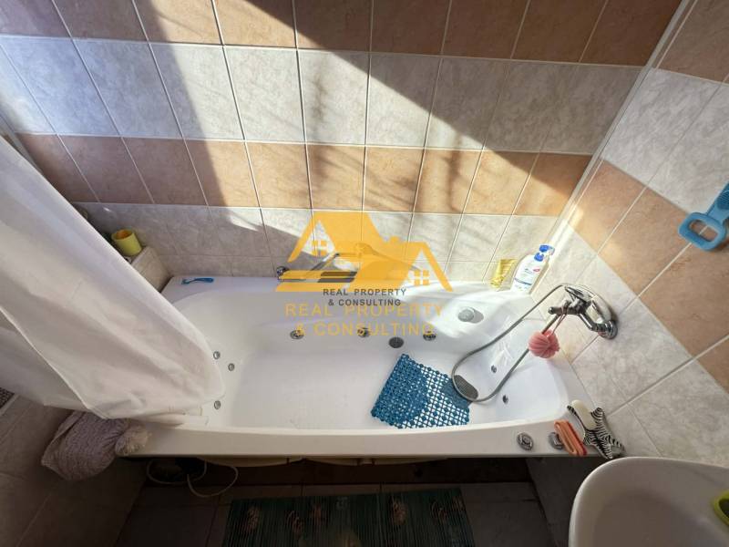 Bathroom with a bathtub in a family house, tiled with beige and white tiles.
