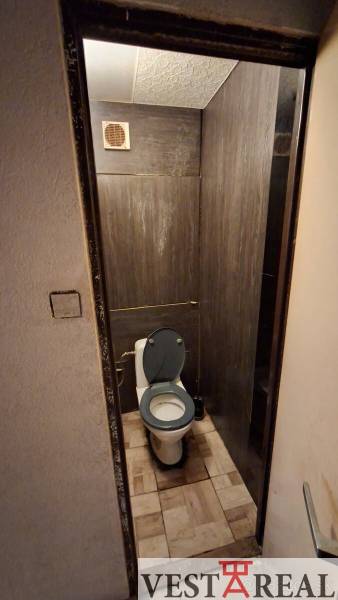 A toilet with ceramic tiles in a 3-room apartment, dark tiling and ventilation.
