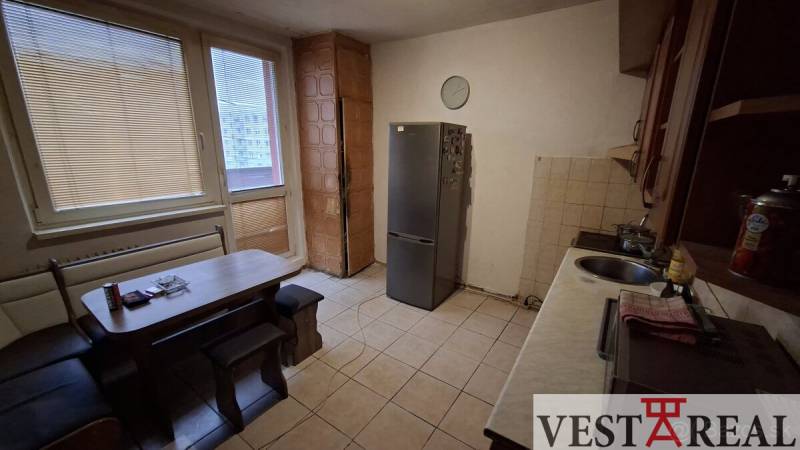 A kitchen in a 3-room apartment with tiles and simple furniture, a refrigerator, and a dining table.