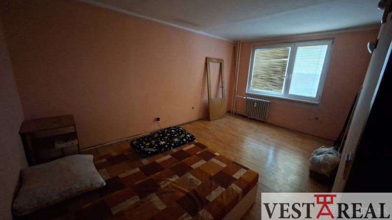 A room with a wooden floor design, a simple bed, and a dresser in a three-room apartment.