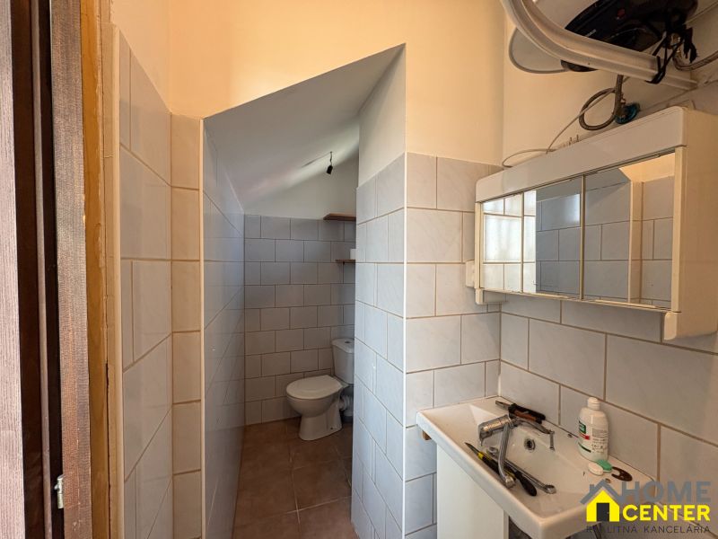 A bathroom in a family house with a sink and a toilet, tiled with light tiles.