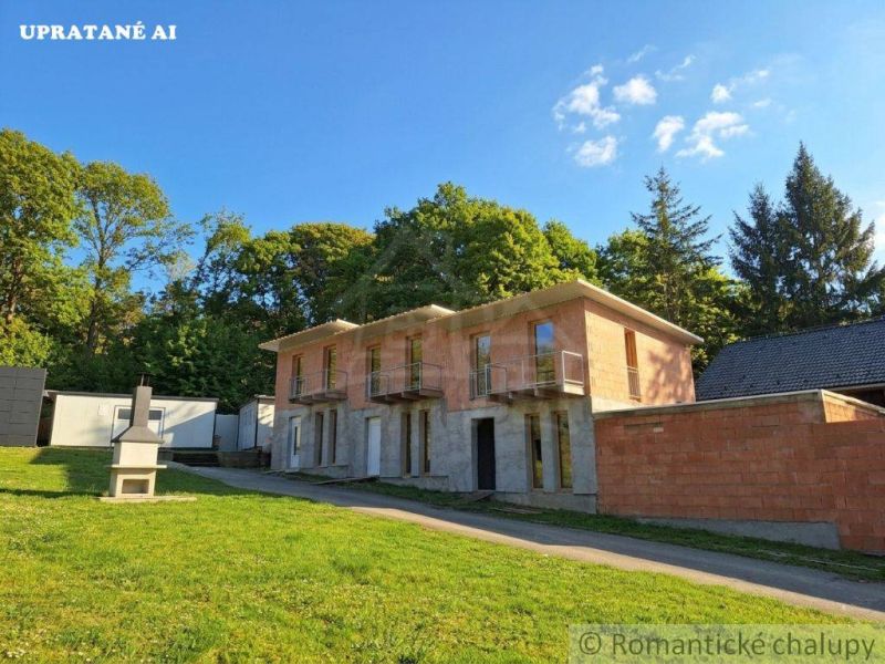A two-story unfinished cottage in Divín surrounded by greenery and a grassy plot.