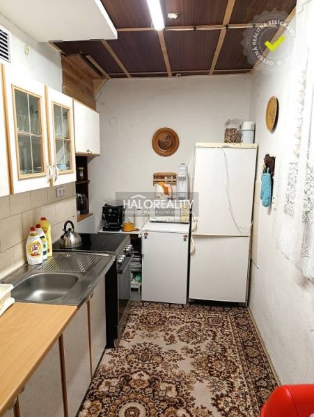 A kitchen in a cottage with simple furnishings, a carpet, and a white refrigerator.