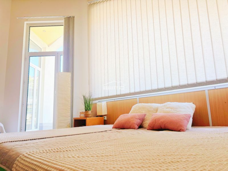 Bright interior of a holiday apartment with a comfortable bed and tall windows.