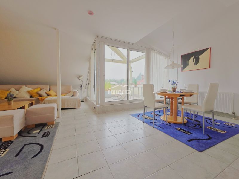 A bright living room of a holiday apartment with a sofa, dining table, and large windows.