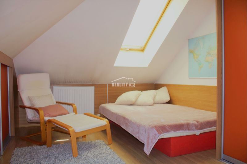 Attic room in a holiday apartment with a bed, chair, and wooden decor flooring.