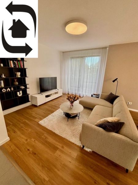 Living room in a two-room apartment with a wooden decor floor, a sofa, and a television.
