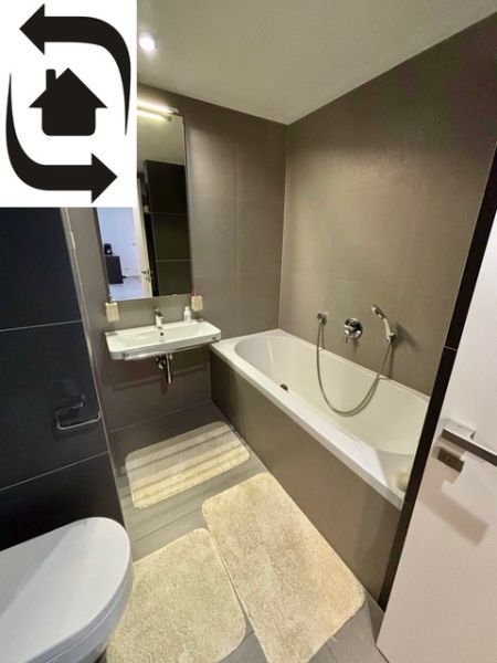 A bathroom in a 2-room apartment with a bathtub, a sink, and beige mats.