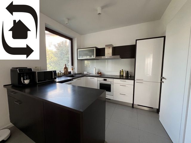 A modern kitchen with a dark countertop in a two-room apartment, equipped with appliances and a large window.
