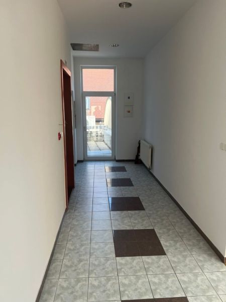 The image shows a bright corridor with a tiled floor leading to an office.