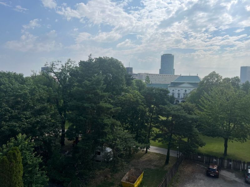 A view of the building among the trees, in the distance Štefánikova Street, behind it offices.