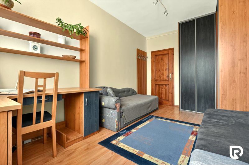 Room in a 3-room apartment with a shelf, gray sofa, and a desk.