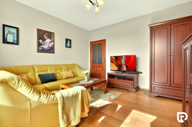 Living room with wood-patterned flooring, yellow sofa, and decorative paintings in a three-room apartment.