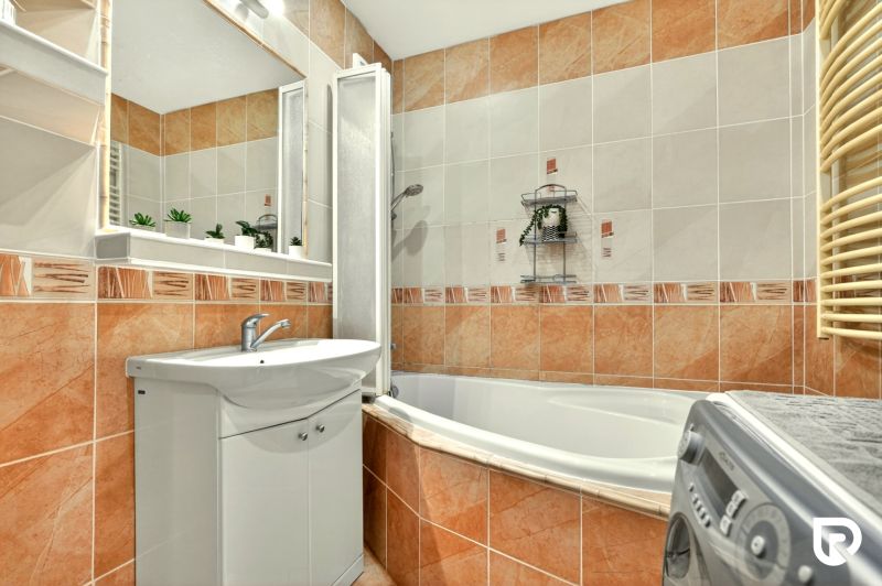 A bathroom in a 3-room apartment with light tiles, a bathtub, and a sink.