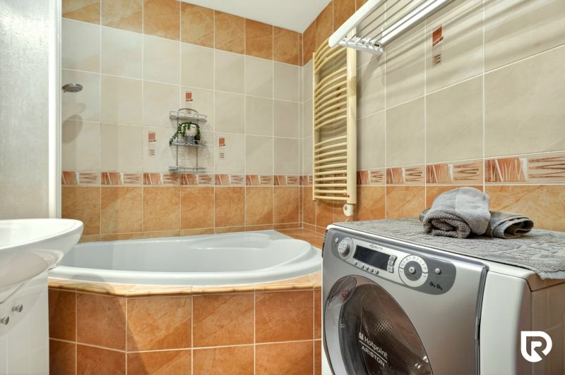 A bathroom in a 3-room apartment with a corner bathtub, washing machine, and clothes dryer.