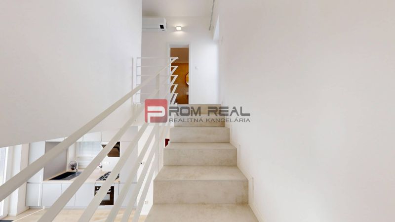 A staircase with white railing and a kitchen in a 3-room apartment.