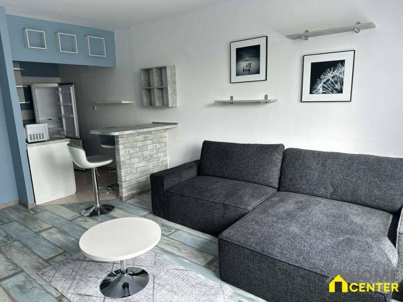 Two-room apartment with wood-patterned flooring, a sofa, and a bar counter.