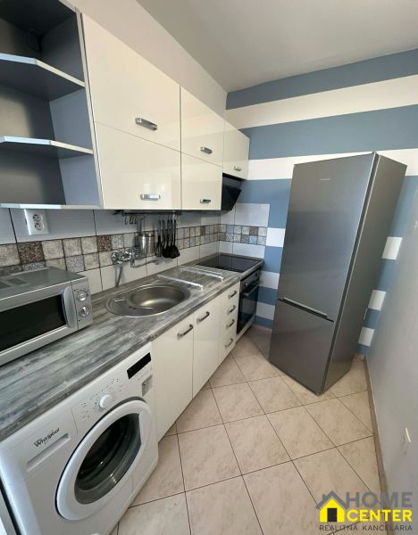 A kitchen in a studio apartment with tiles, a kitchen unit, appliances, and a striped wall.