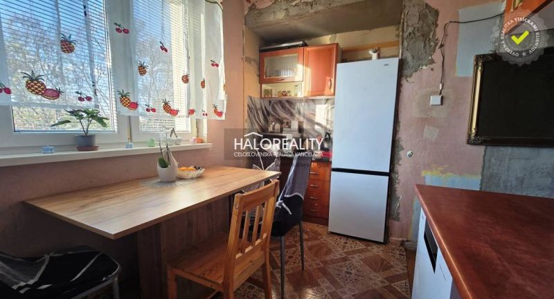 A kitchen in a 3-room apartment with a wooden table, refrigerator, and decorative curtains.