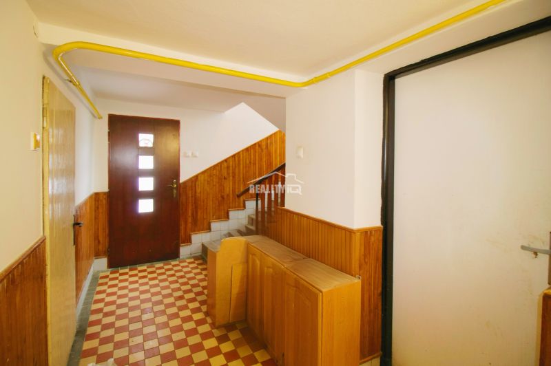 A hallway in a family house with stairs, tiled floor, and wall cladding.