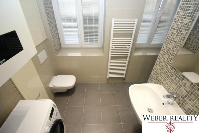 Bathroom in a 2-room apartment with a washing machine, shower, and window with blinds.