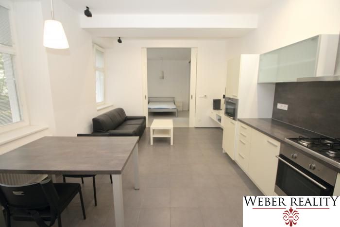 Living room and kitchen in a 2-room apartment with dark furniture and built-in appliances.