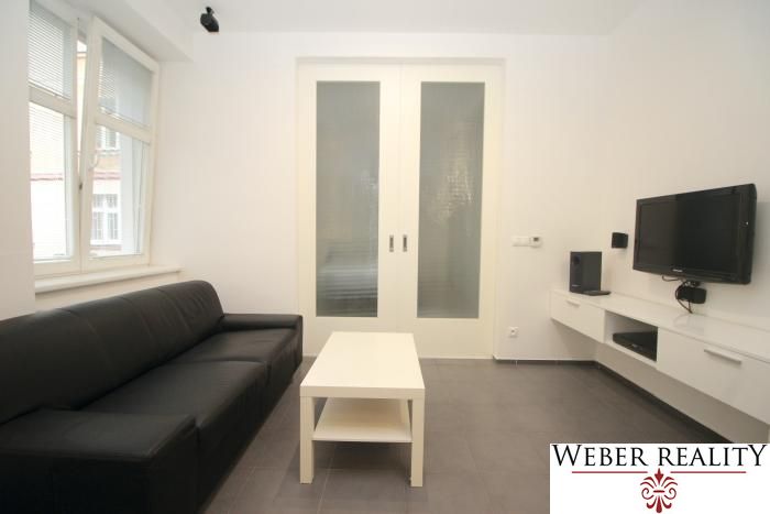 Living room in a two-room apartment with a dark sofa and a TV on the wall.