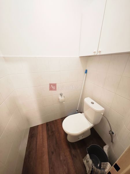 A toilet with tiles and a wooden decor floor in a 2-room apartment.