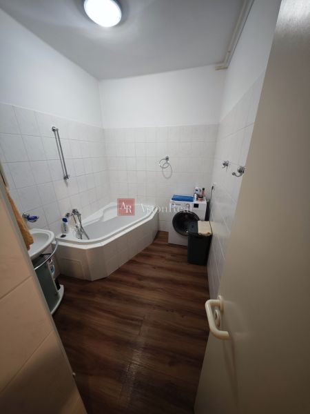 A bathroom in a 2-room apartment with a corner bathtub and a floor with a wooden decor.