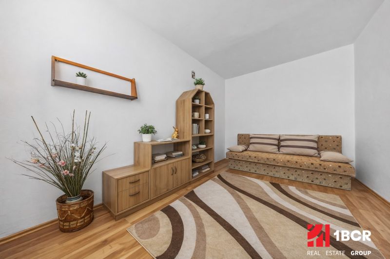 Living room with a sofa, wooden furniture, and a floor with a wood pattern in a three-room apartment.