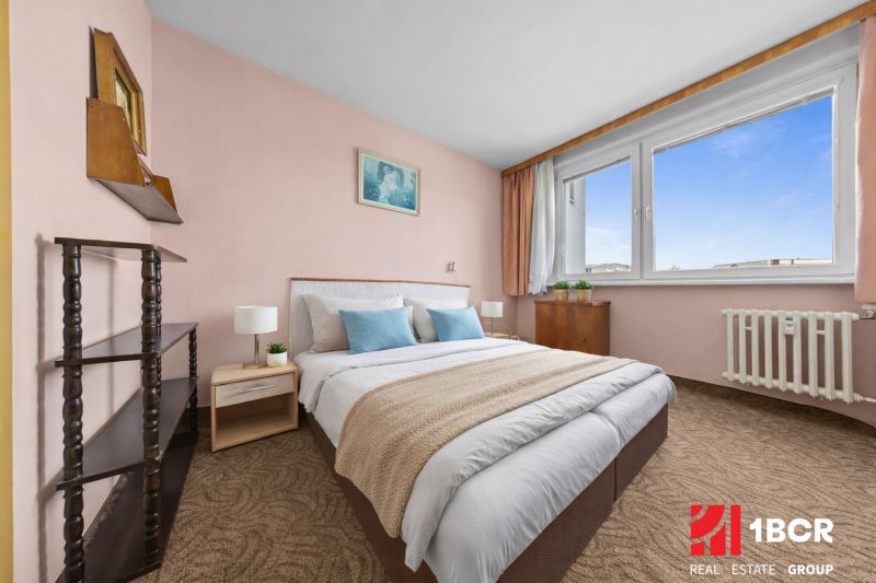 A bedroom in a 3-room apartment with carpet flooring, light walls, and large windows.