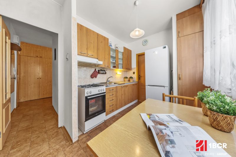 A kitchen in a 3-room apartment with a wooden decor floor and light furniture.