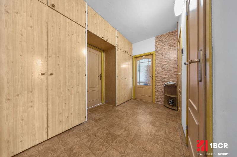 A hallway with built-in wardrobes, tiles, and a brick wall in a 3-room apartment.