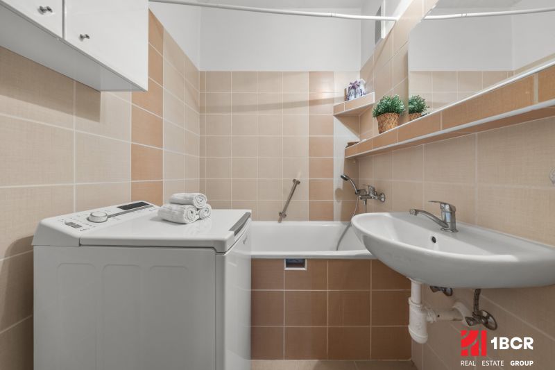 Bathroom with a washing machine in a 3-room apartment, beige tiles, sink, bathtub, shelves.