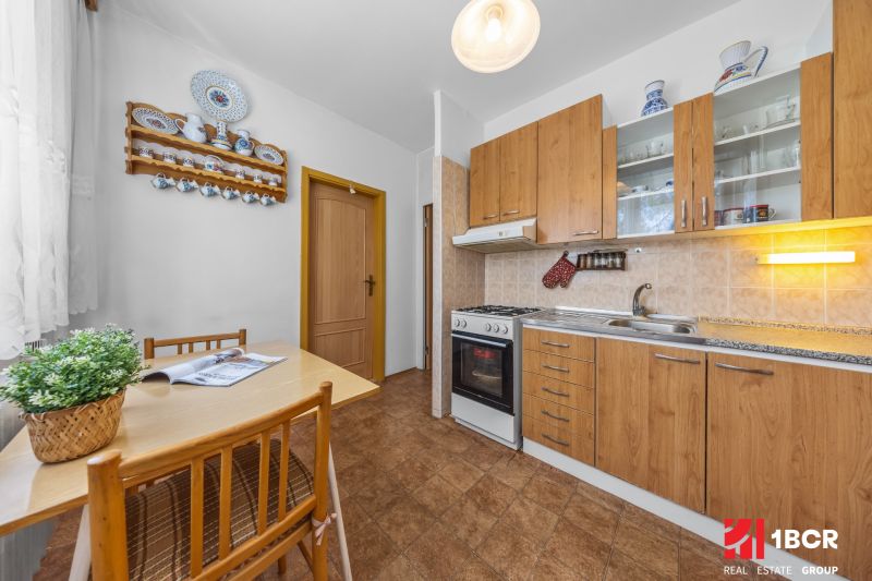 A kitchen in a 3-room apartment with a kitchenette, wood decor, and a dining table with chairs.
