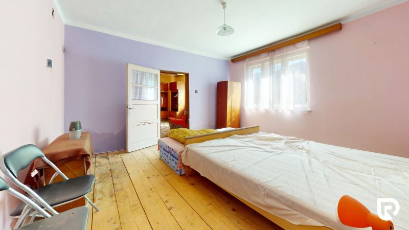 Bedroom in a family house with a bed, wood-patterned flooring, and light pink walls.