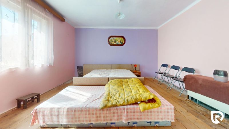 A bedroom in a family house with a yellow blanket, folding chairs, and a wooden decor floor.