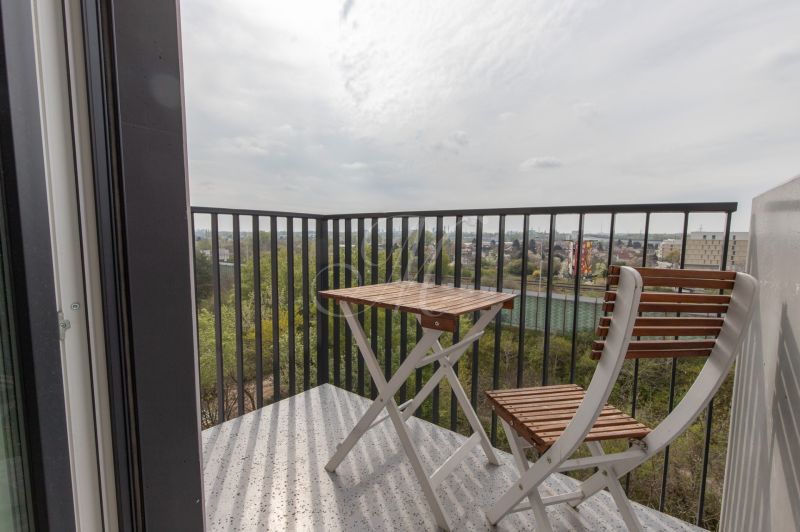 A balcony with wooden chairs and a table in a 2-room apartment with a view of the countryside.