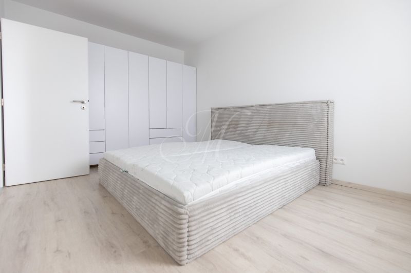 Bedroom in a two-room apartment with wood-patterned flooring, built-in wardrobe, and bed.