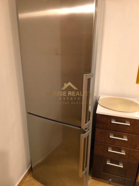 A stainless steel refrigerator in the corner of the kitchen of a three-room apartment with an adjacent wooden sideboard.