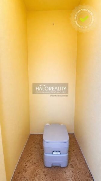 A dry toilet in a yellow room with walls without doors and a floor with a wooden decor.