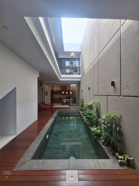 Swimming pool in a villa, with a wooden decor floor, surrounded by houseplants.