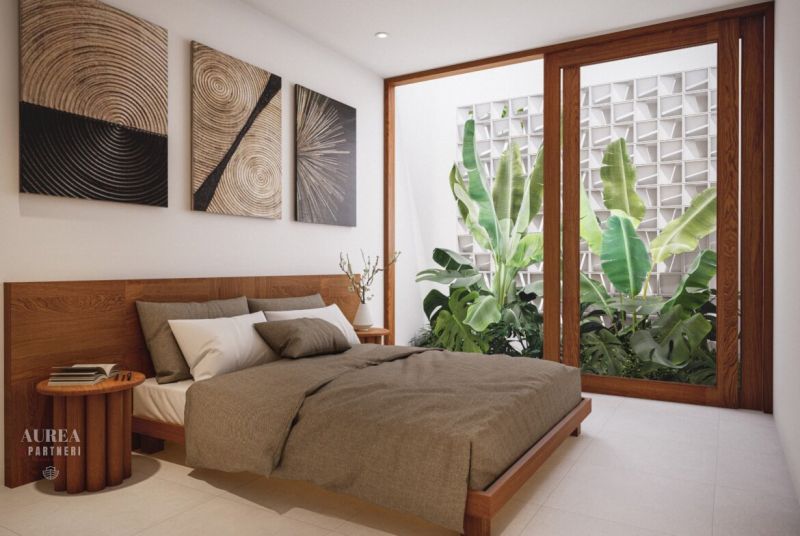 A bedroom in a villa with plants behind large windows and artworks on the wall.