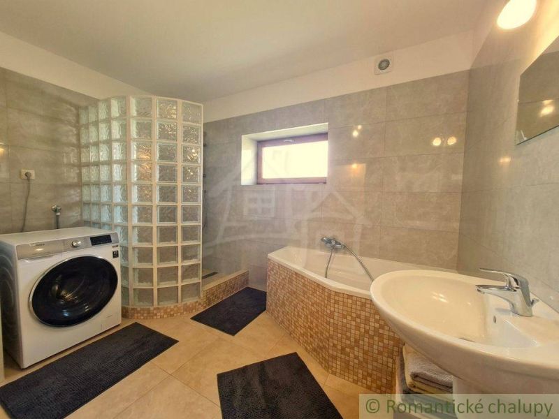 A bathroom in a family house with a bathtub, a washing machine, and a glass block shower.