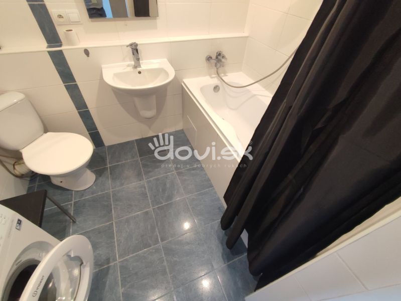 A bathroom in a studio apartment with a sink, bathtub, washing machine, and toilet.
