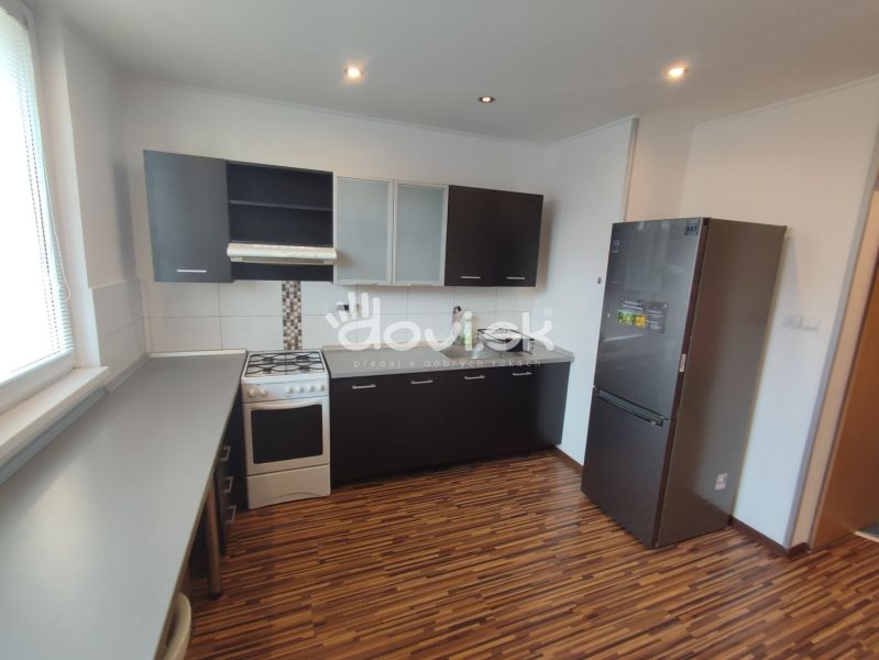 A kitchen in a studio apartment with black kitchen cabinets, a white stove, and a wooden-patterned floor.