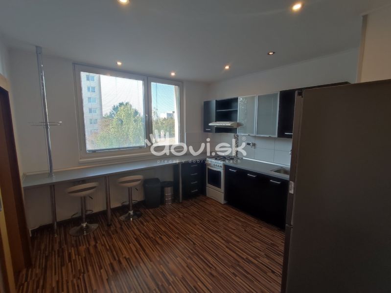 A kitchen in a studio apartment with black cabinets and a wood-patterned floor.